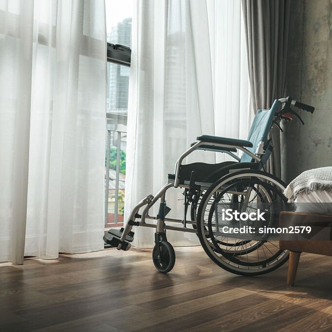 leerer Rollstuhl steht zum Fenster mit weißen Vorhängen gedreht in einem Schlafzimmer