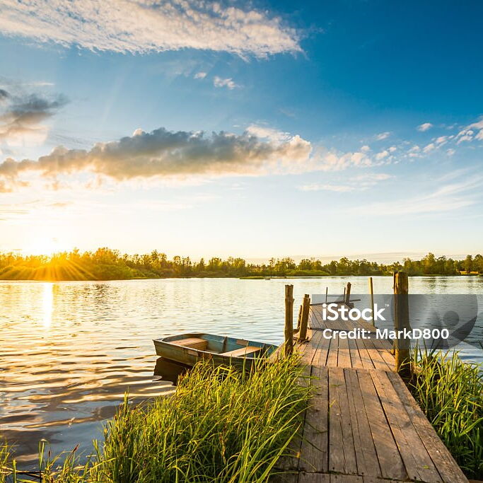 Hozsteg zu einem See mit Sonnenuntergang führend, ein Holzboot zur linken Seite schwimmend