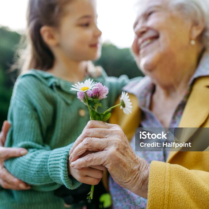 eine alte Dame hält die Hand eines Mädchen, gemeinsam halten sie selbstgepflückte Blumen